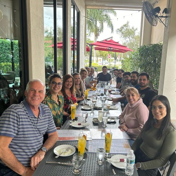 A group of people enjoying a meal together at a long table on the outdoor patio of Aromas del Peru.