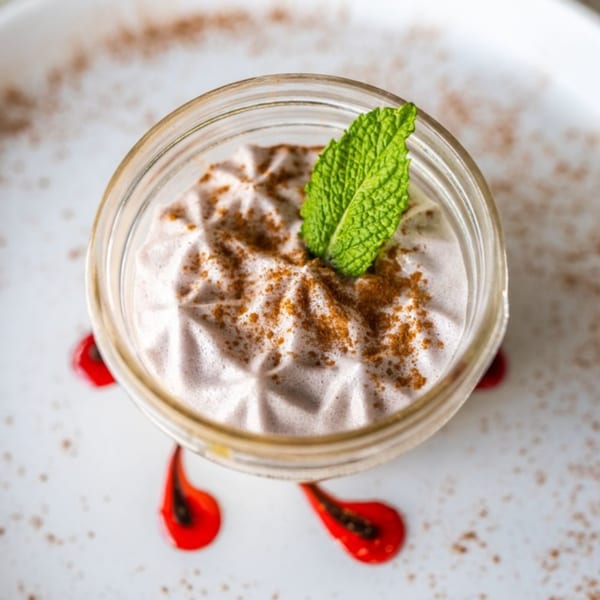 Peruvian dessert Suspiro de Lucuma, a creamy mousse with cinnamon and mint, on a white plate.
