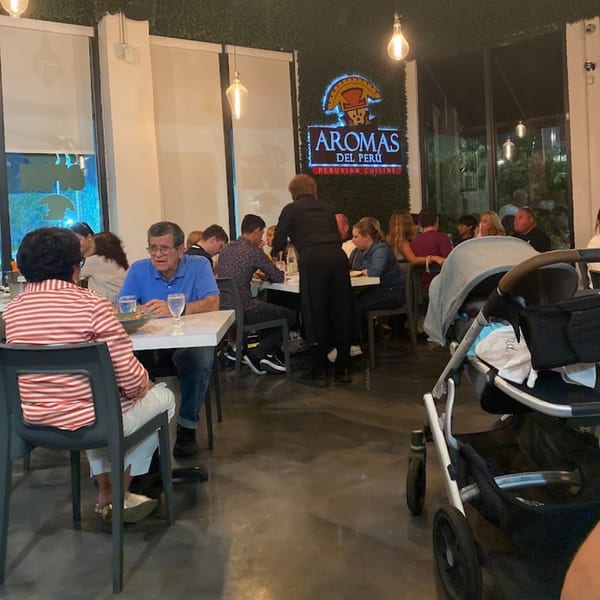 Diners seated at tables in Aromas del Peru restaurant, with a server attending to guests and a baby stroller nearby.