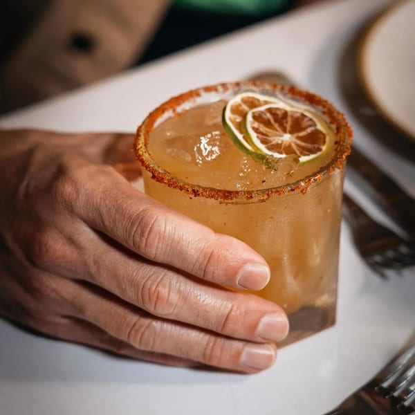 Hand holding a Peruvian cocktail with a chili-salted rim and dried lime garnish.
