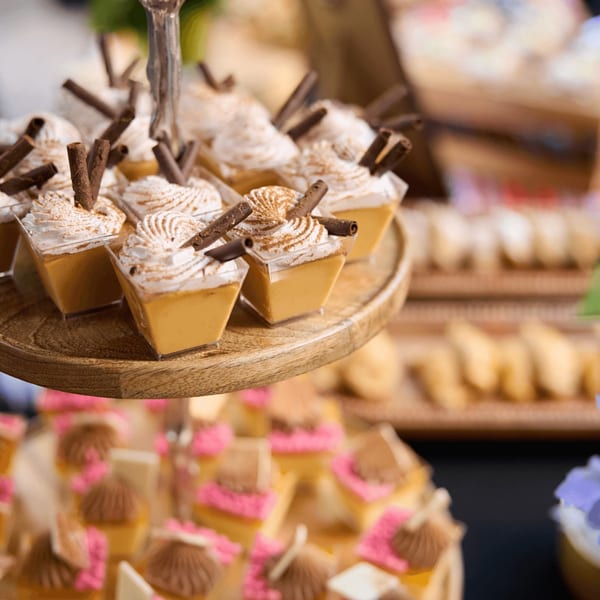 Dessert cups with whipped cream and chocolate sticks on a wooden tiered stand.