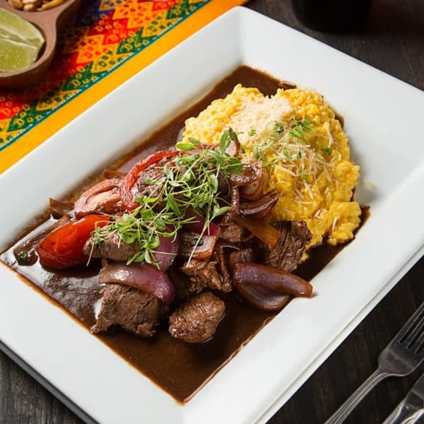 Peruvian Lomo Saltado with beef, red onions, tomatoes, and yellow rice, garnished with microgreens.