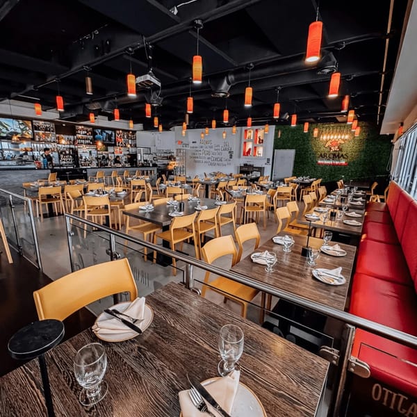 Interior of Aromas del Peru restaurant with red pendant lights, wooden tables, yellow chairs, and a bar.