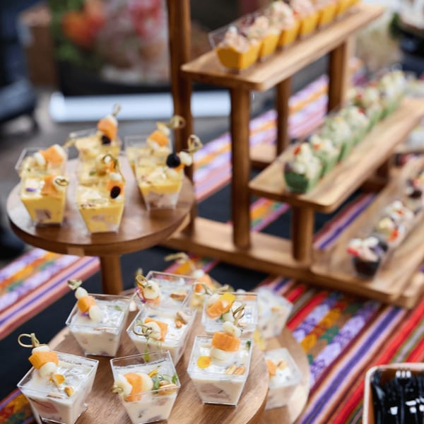 A vibrant display of Peruvian appetizers, including ceviche and causa, on tiered wooden stands.