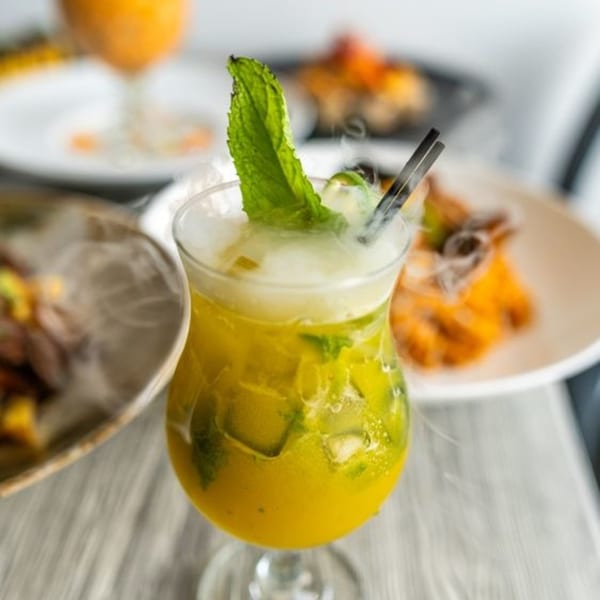 A Peruvian cocktail with mint and dry ice smoke, with blurred dishes in the background.