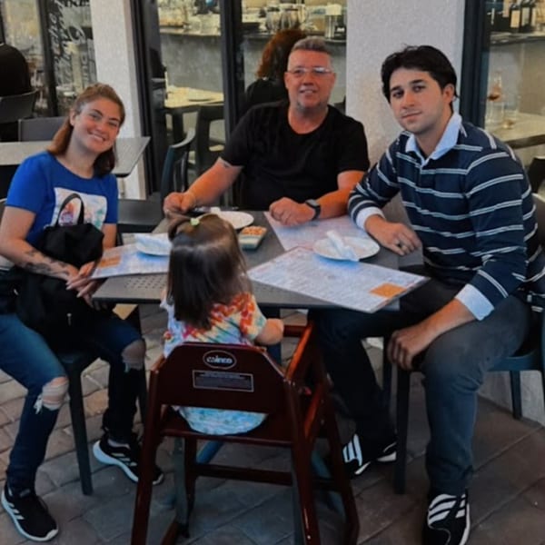 A family of four, including a toddler in a high chair, seated at an outdoor table at Aromas del Peru.