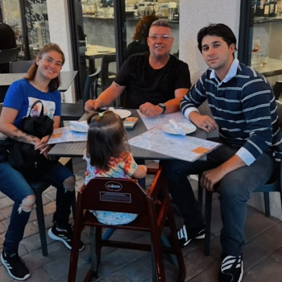 A family of four, including a toddler in a high chair, seated at an outdoor table at Aromas del Peru.