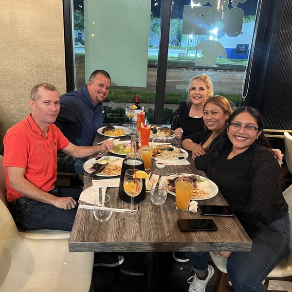 Five smiling people enjoying Peruvian dishes and drinks at a restaurant table at night.