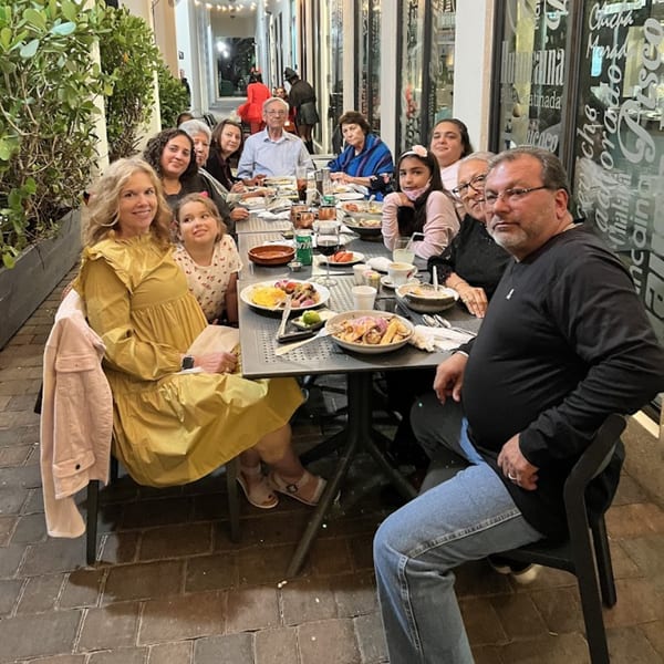 A large family group enjoys Peruvian dishes and drinks at an outdoor table at Aromas del Peru.