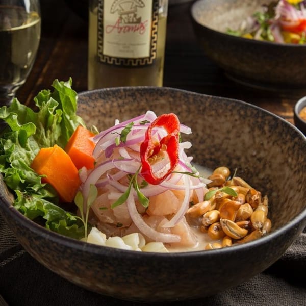 Peruvian ceviche with fish, red onions, corn, sweet potato, and lettuce, with a wine bottle in the background.