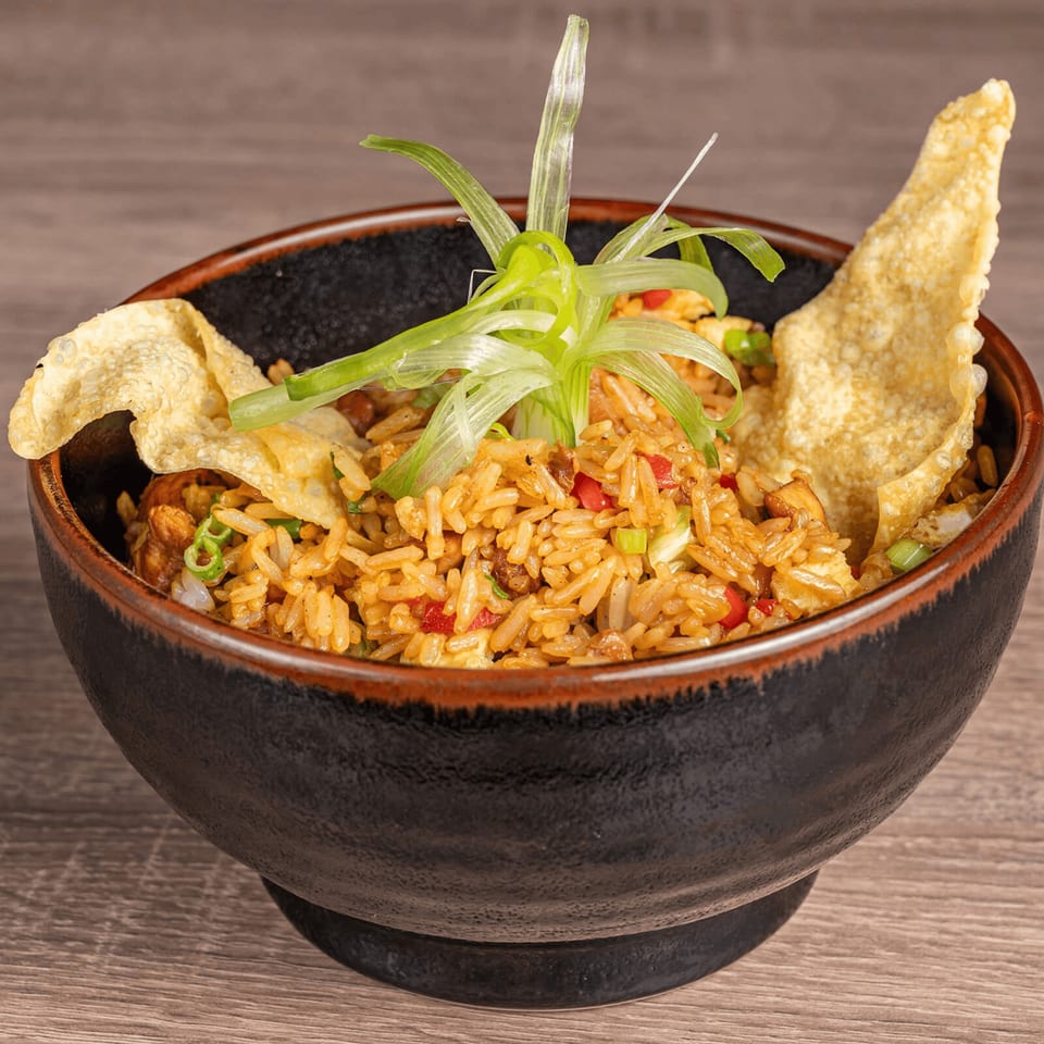 Peruvian fried rice (Arroz Chaufa) in a dark bowl, garnished with green onions and wonton crisps.