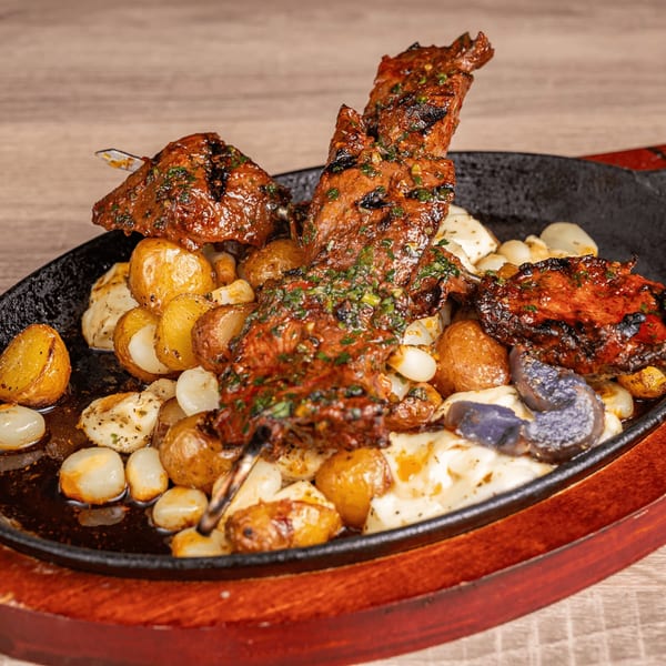 Peruvian anticuchos with roasted potatoes, white corn, and purple potatoes on a sizzling platter.