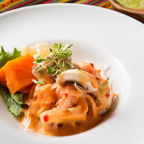 Peruvian ceviche with salmon, mushrooms, sweet potato, corn, and lettuce in a white bowl.