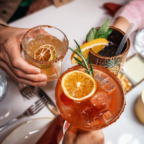 Three vibrant cocktails, two garnished with citrus and chili rim, one with mint and orange.