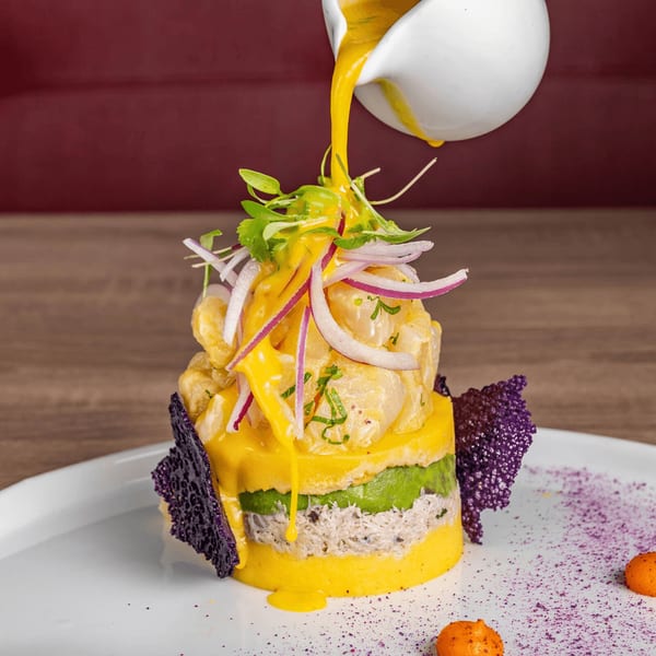 Aromas del Peru's causa, a layered Peruvian dish with yellow potato, avocado, crab, and ceviche, topped with a yellow sauce.