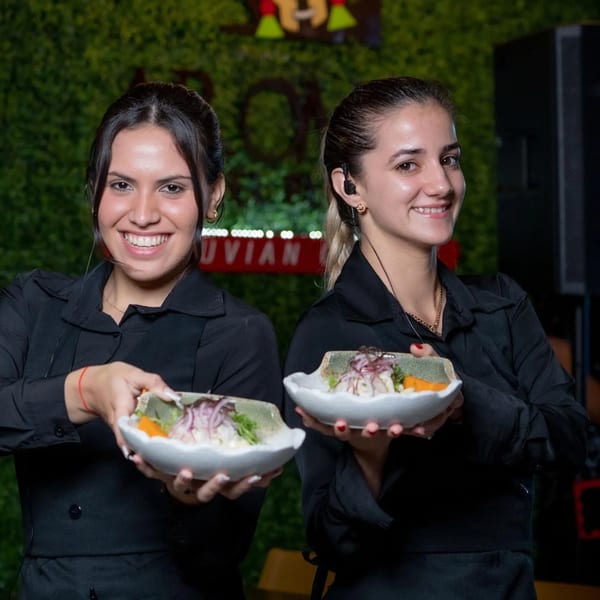 Two smiling waitresses from Aromas del Peru present bowls of fresh Peruvian ceviche.