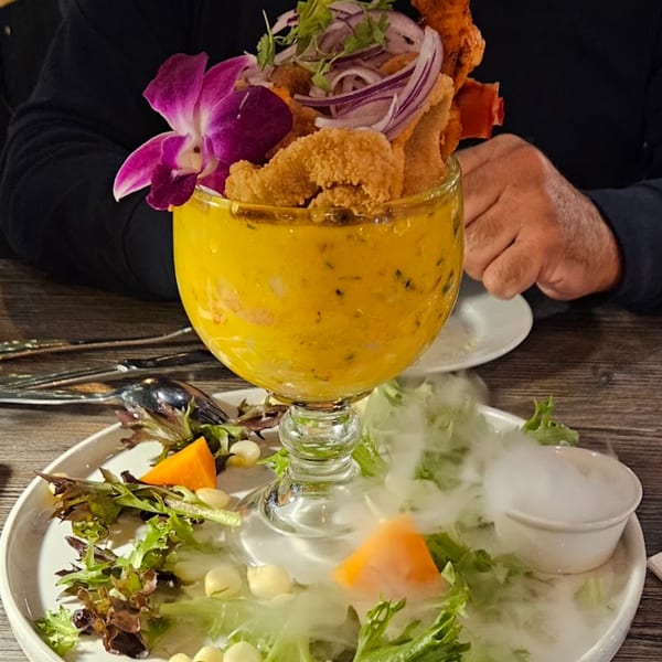 Aromas del Peru's Peruvian ceviche in a large glass, garnished with fried seafood, red onions, and an orchid.