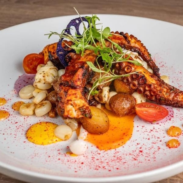 Grilled octopus with potatoes, corn, tomatoes, and sauces on a white plate at Aromas del Peru.